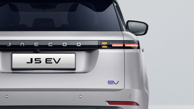 Bagfra ses en sølvfarvet JAECOO J5 elbil med baglygte, bagskilt og EV-emblem på en lys baggrund.
