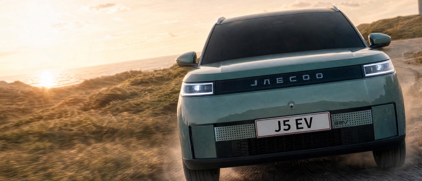 En grøn JAECOO el-SUV med nummerpladen J5 EV kører ad en grusvej ved solnedgang.